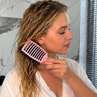 Jeune femme aux longs cheveux mouillés châtains qui brosse ses cheveux avec la brosse à cheveux rose