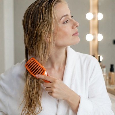 Jeune femme aux longs cheveux châtains clairs qui brosse ses cheveux avec la brosse à cheveux de couleur orange
