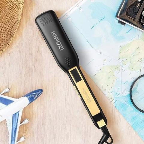 lisseur noir posé sur un plan en bois avec accessoires décoratifs de voyage à côté