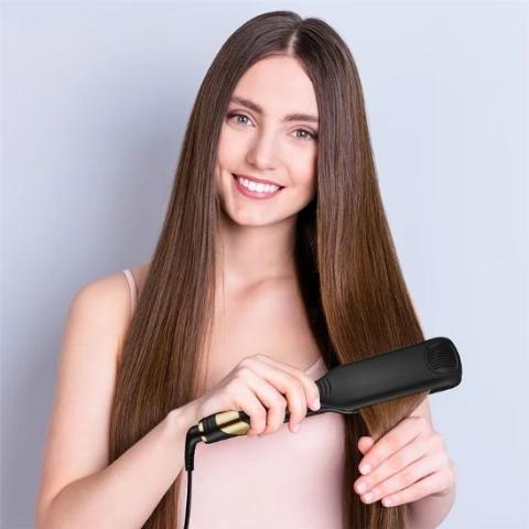 Jeune femme d'environ 20-25 ans longs cheveux bruns qui se coiffe avec le lisseur