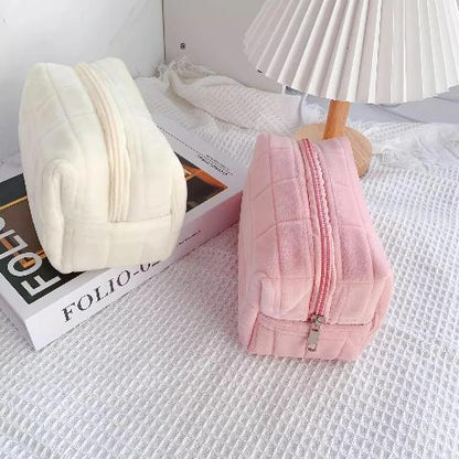 Trousse de toilette creme et rose posées sur un plan décoratif blanc