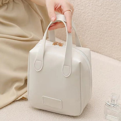 une main qui tient la trousse de toilette couleur blanche afin d'en apprécier les caractéristiques