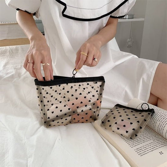 Une main de femme qui place un accessoire de maquillage dans la trousse de toilette petits coeurs couleur beige 
