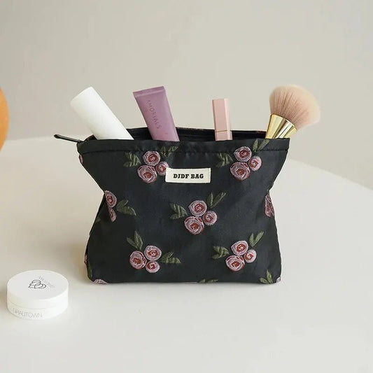 Trousse de toilette pochette couleur noire et rose posé sur un plan crème