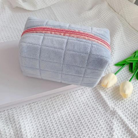 Trousse de toilette couleur bleue posée sur un plan décoratif blanc avec des tulipes à côté