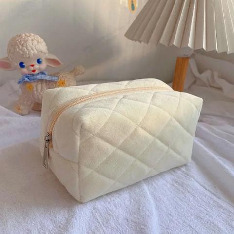 Trousse de toilette velours couleur crème posée sur un drap décoratif blanc