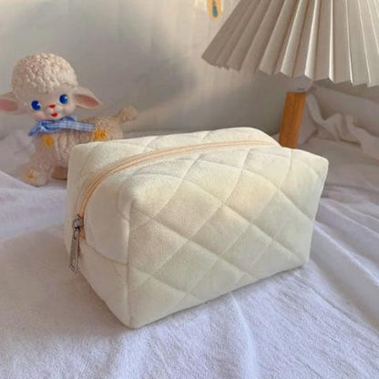 Trousse de toilette velours couleur crème posée sur un drap décoratif blanc
