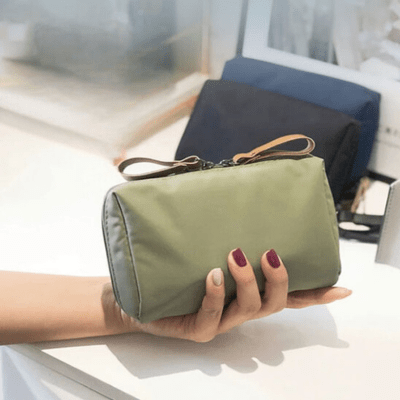 Une femme qui tient la trousse de toilette mini pochette couleur verte afin d'en apprécier toutes les caractéristiques