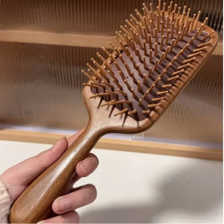 une main qui tient la brosse à cheveux bois de santal 