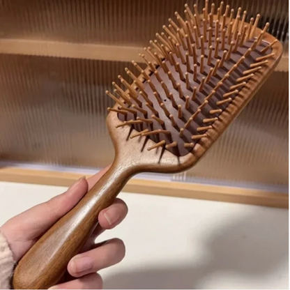 une main qui tient la brosse à cheveux bois de santal 